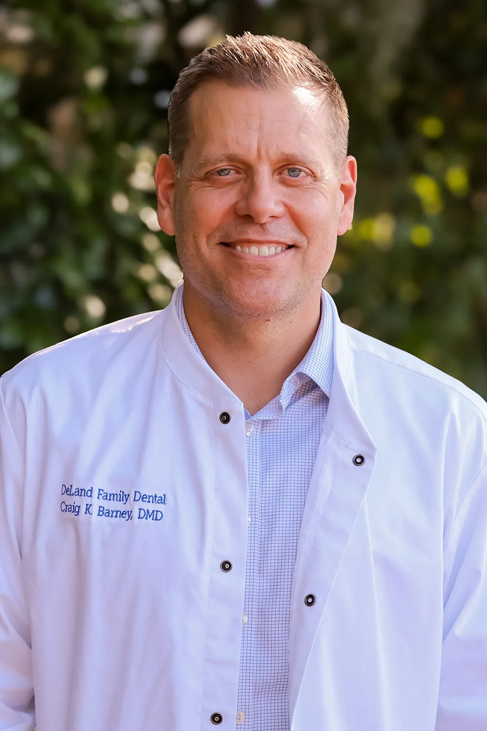 Dr. Craig Barney, DMD of DeLand Family Dental, smiling outdoors in a white dental coat.