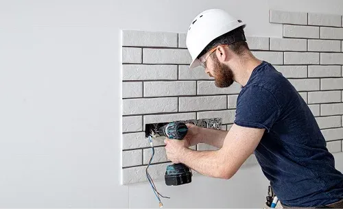 A residential electrician in Anaheim, CA installing installing new electrical wiring for electrical outlets in a residential setting, wearing a hard hat and using a power drill, emphasizing safety and professional service