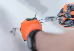 close up of an electricians hands wearing safety gloves while installing electrical wiring and using electrical pliers to trip the new electrical wiring