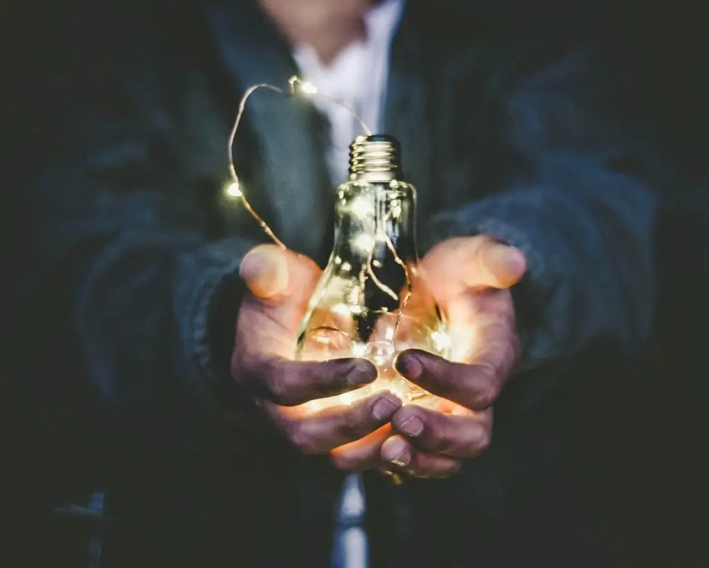 Hands holding a glowing light bulb, symbolising ideas and insights in coaching.
