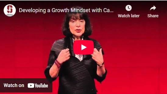 Woman speaking on stage about growth mindset, with a YouTube play button overlay. Background is red.