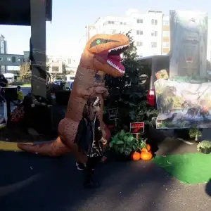 Person in T-Rex costume and child in superhero costume next to Jurassic Park car.
