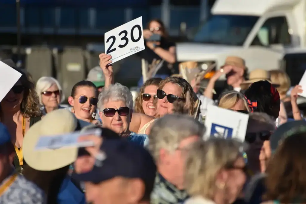 Many people at an outdoor auction, a hand holding paddle number 230.