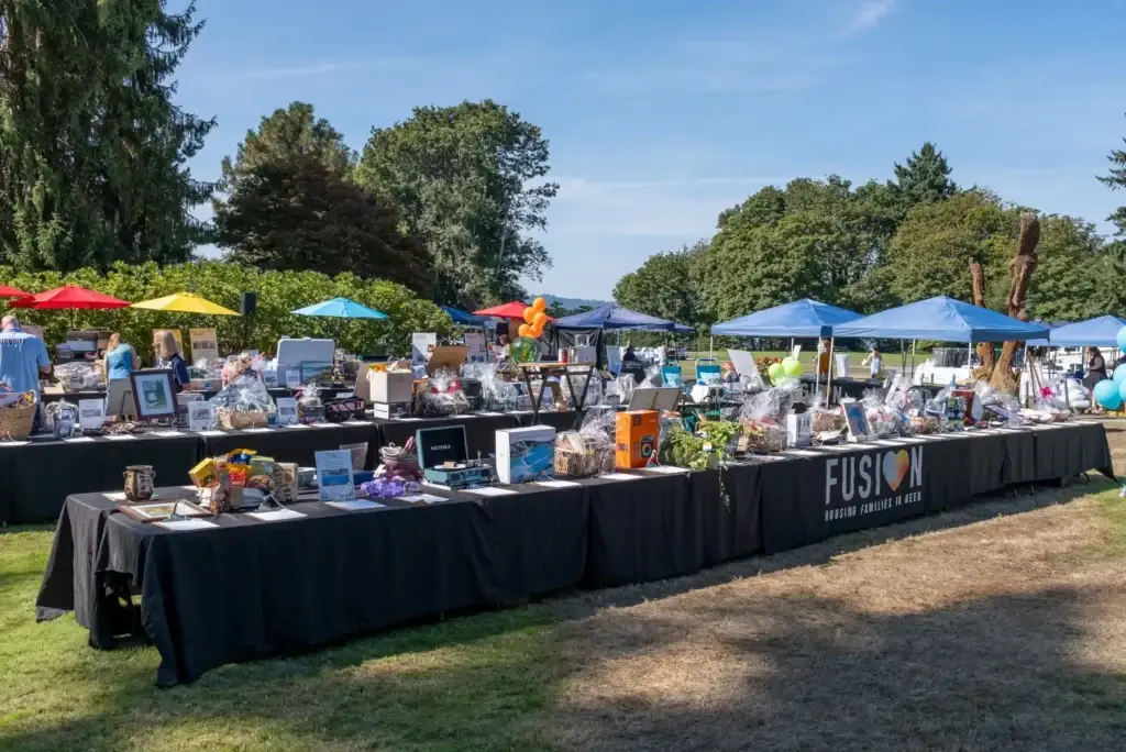 FUSION outdoor fundraiser: long tables with auction items under colorful umbrellas and blue tents.