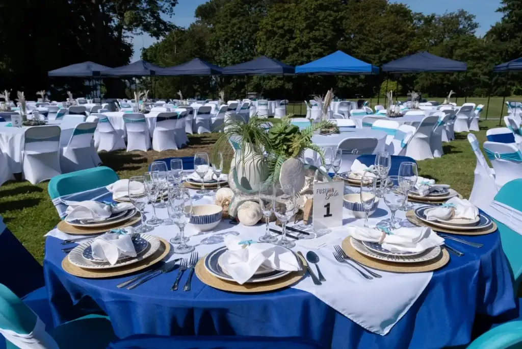 Gala tables outdoors, decorated in blue/teal with shells, plants, and shaded tents.