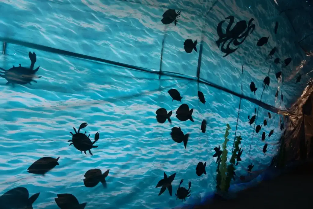 Wavy blue tunnel adorned with black silhouettes of fish, crabs, an octopus, and jellyfish.