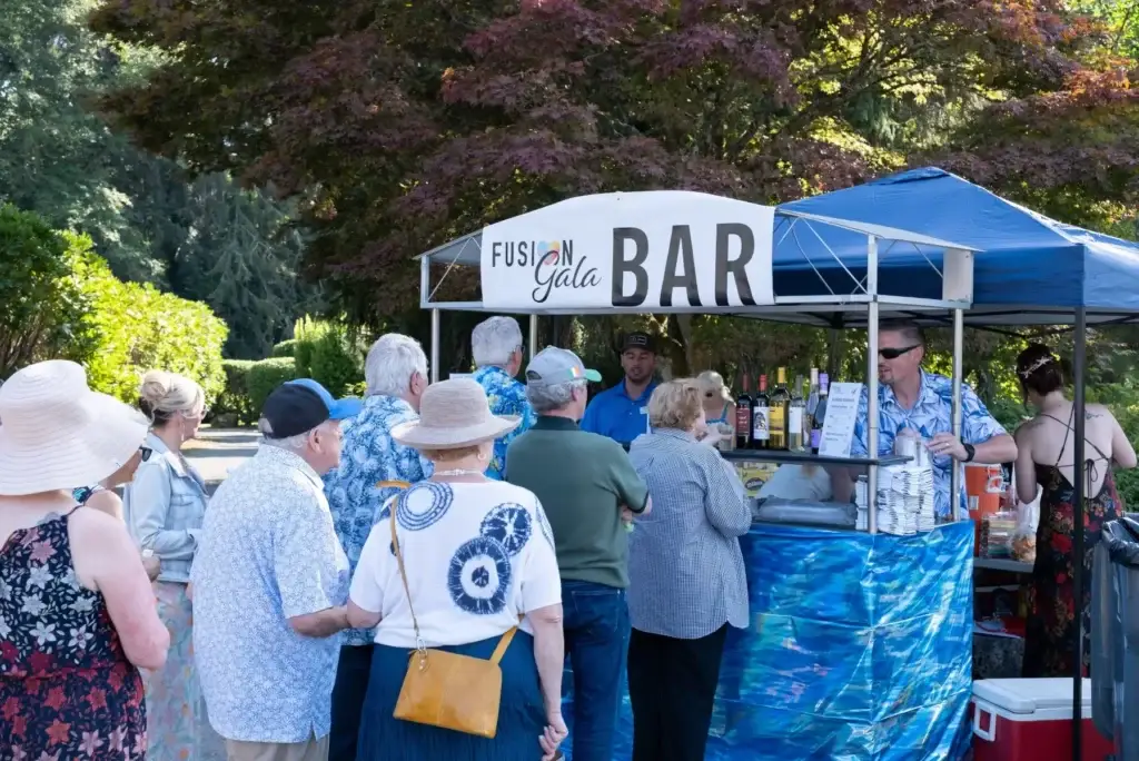 Attendees order drinks at an outdoor "Fusion Gala Bar" under lush trees.