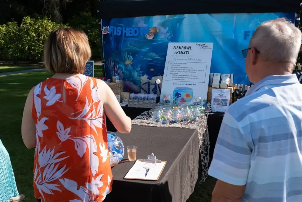 People view a colorful Fishbowl Frenzy game stall with an underwater backdrop outdoors.