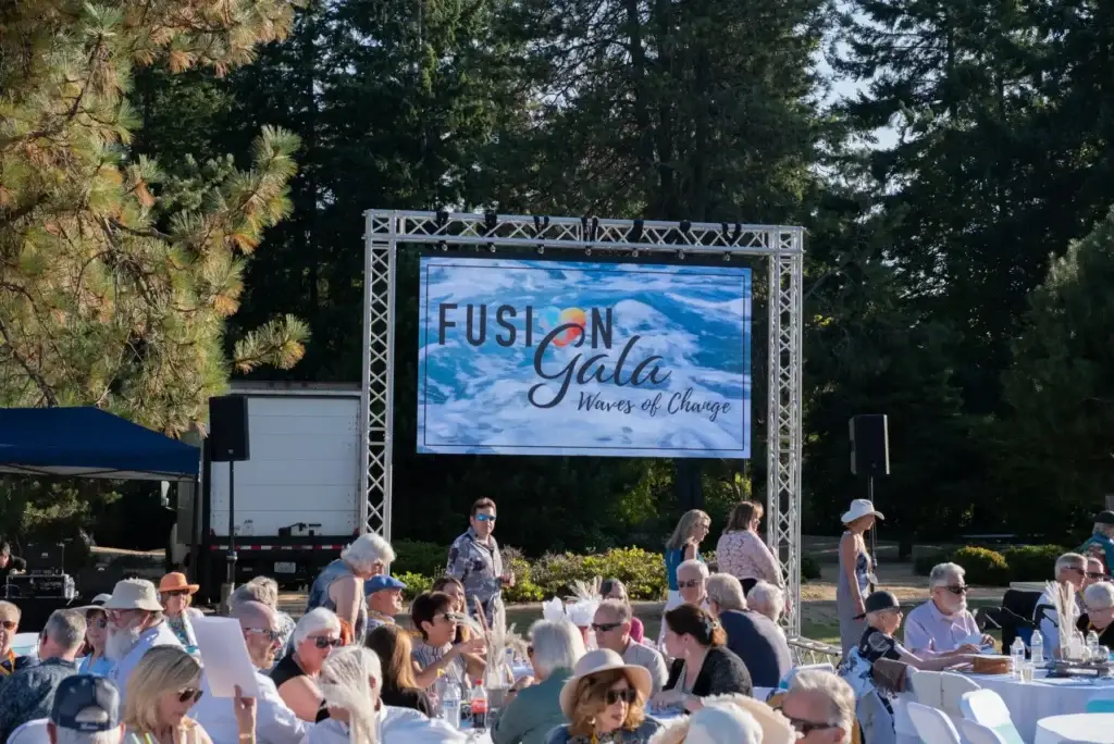 Outdoor "Fusion Gala: Waves of Change" event with guests and a large LED screen.