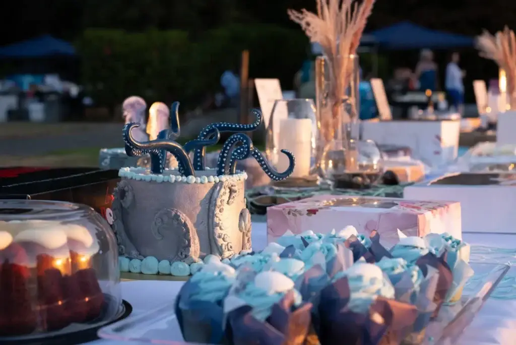 Octopus tentacle cake and blue cupcakes on a dessert table at a sunset outdoor event.