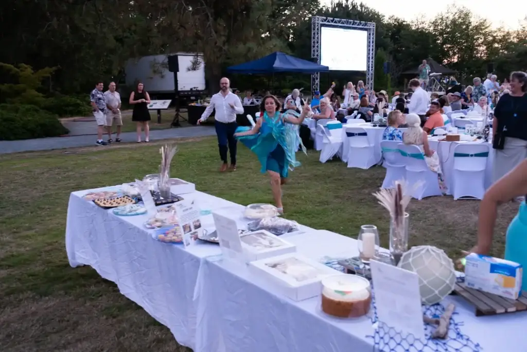 Woman in a flowing blue dress dances at a festive outdoor evening event with dessert tables.