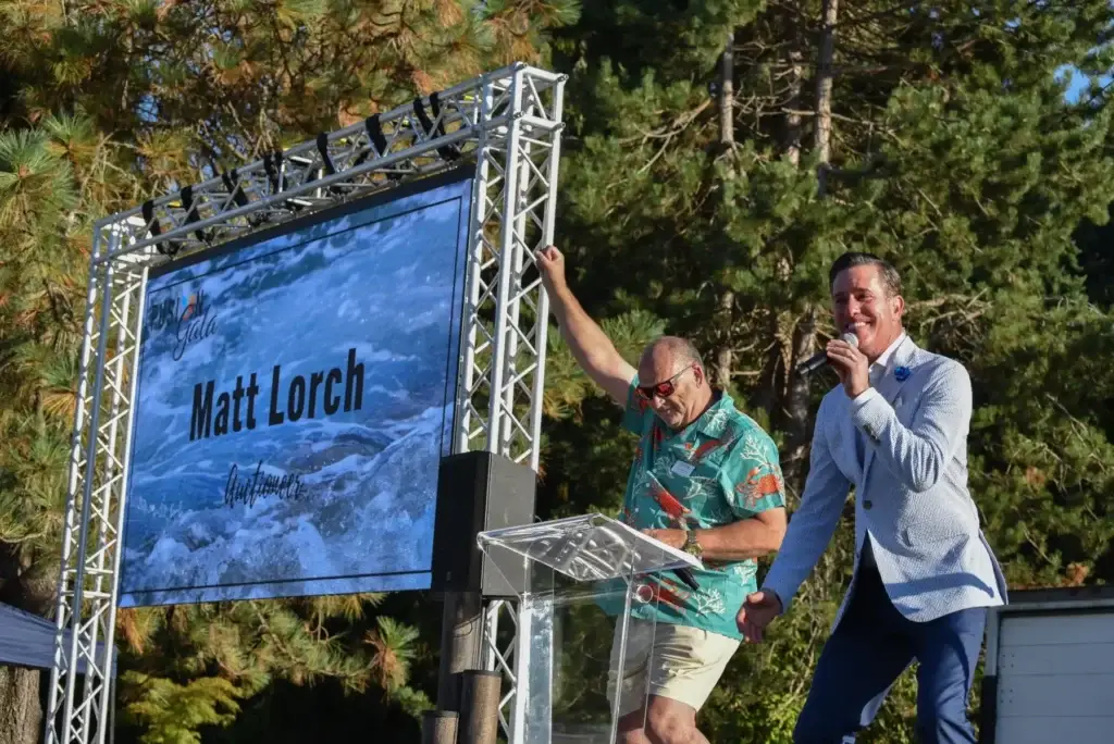 Outdoor stage event: Man raises fist, man speaks, "Matt Lorch" on large screen.