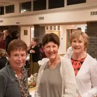 Three smiling women at a festive indoor gathering.