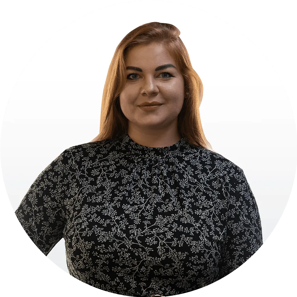 Aleksandra Równiak-Kaczmarek A woman with long red hair wearing a black dress with a white floral pattern stands confidently against a plain white background, framed by a circular border.