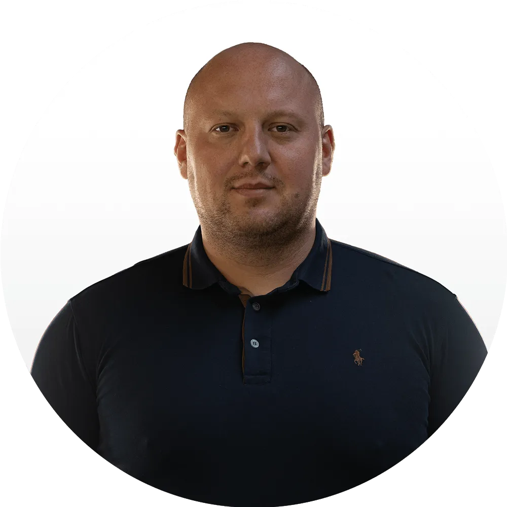 Jakub Pochopień A man with a shaved head wearing a dark navy polo shirt stands against a plain white background, representing the Good Stuff team as he faces the camera with a neutral expression.
