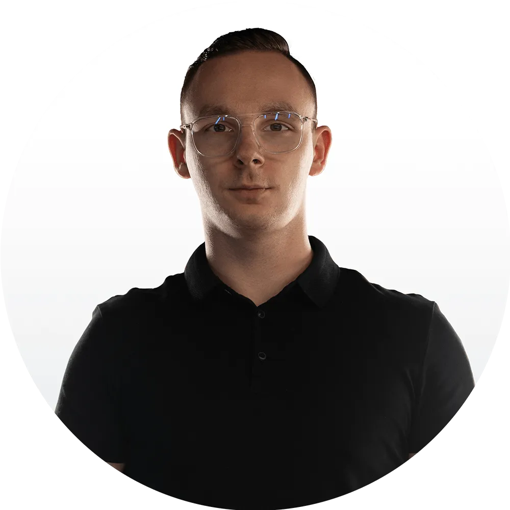 Nikodem Kokoszanek A young man with short brown hair, wearing clear eyeglasses and a black collared shirt, stands against a plain white background, looking directly at the camera.