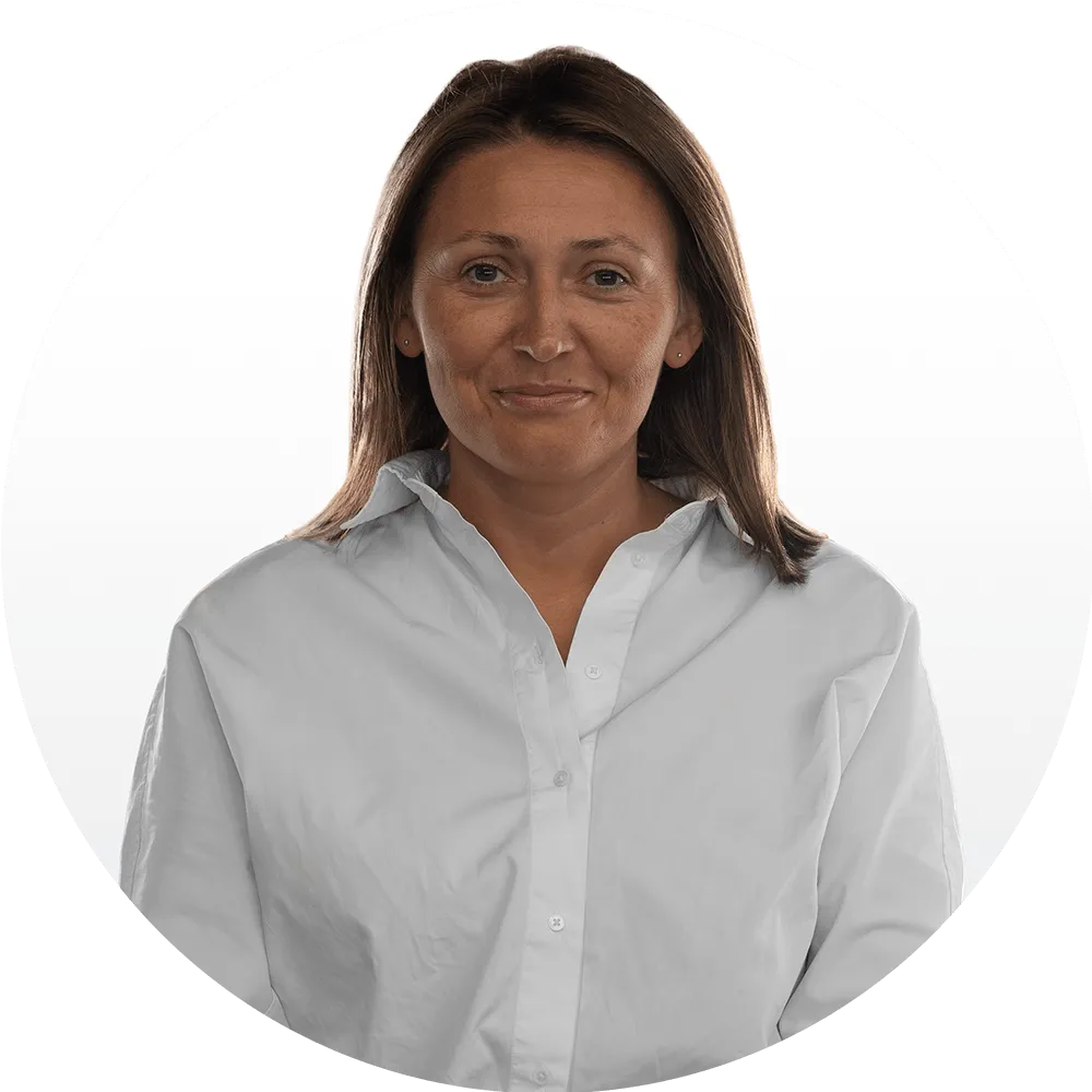 Żaneta Śrama Woman with straight brown hair wearing a white button-up shirt, standing against a plain white background, looking directly at the camera with a slight smile.