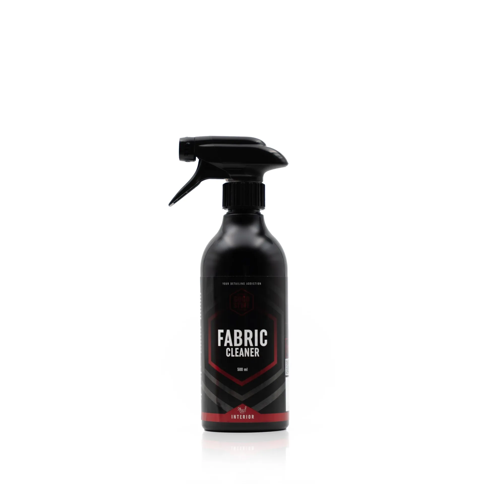 A black spray bottle labeled Fabric Cleaner stands upright against a plain white background. The label features red and white accents and highlights its use for interior car care near the bottom.