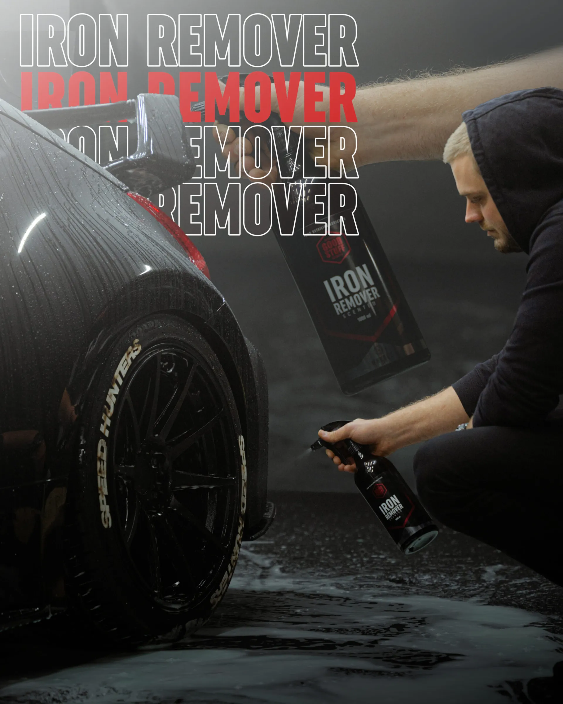 Mężczyzna rozpyla Good Stuff Iron Remover, skuteczny środek do felg, na kierownicę czarnego samochodu. Napis "IRON REMOVER" pojawia się odważnie w tle. Mokra, spieniona opona pokazuje jego skupienie na czyszczeniu i usuwaniu osadów metalicznych.