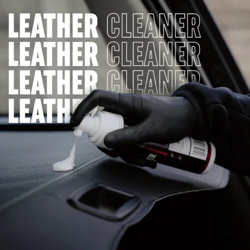 A gloved hand sprays white leather cleaner foam onto a car's dashboard, showcasing effective leather car care. The words LEATHER CLEANER repeat in bold white and black text on both sides of the image.