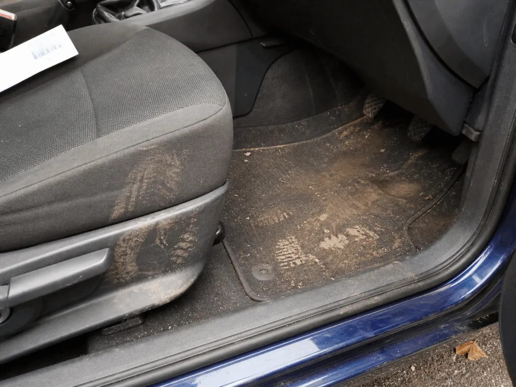 The photo shows the dirty interior of a car, focusing on the floormat and seat. Muddy footprints and dirt are visible—perfect candidates for a deep clean with the best car shampoo from our latest car shampoo guide.