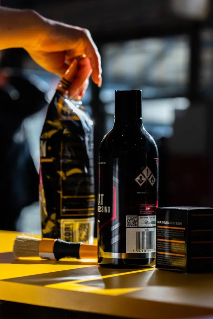 Una mano coloca una bolsa transparente con productos de aseo personal sobre una superficie amarilla, junto a un frasco, un cepillo y una cajita, todo ello iluminado por la luz del sol.
