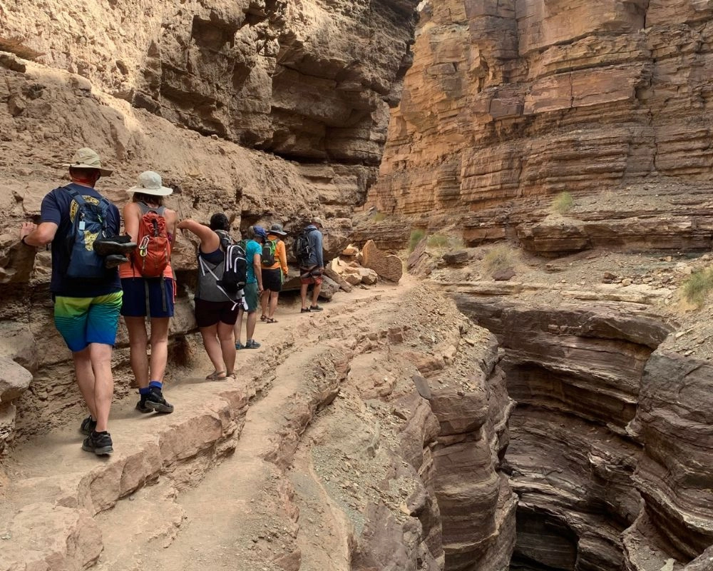 Side Hikes on a Grand Canyon River Trip: What You Need to Know 4 Hiking along a narrow ledge through Deer Creek Canyon to reach The Patio oasis above the Colorado River in Grand Canyon