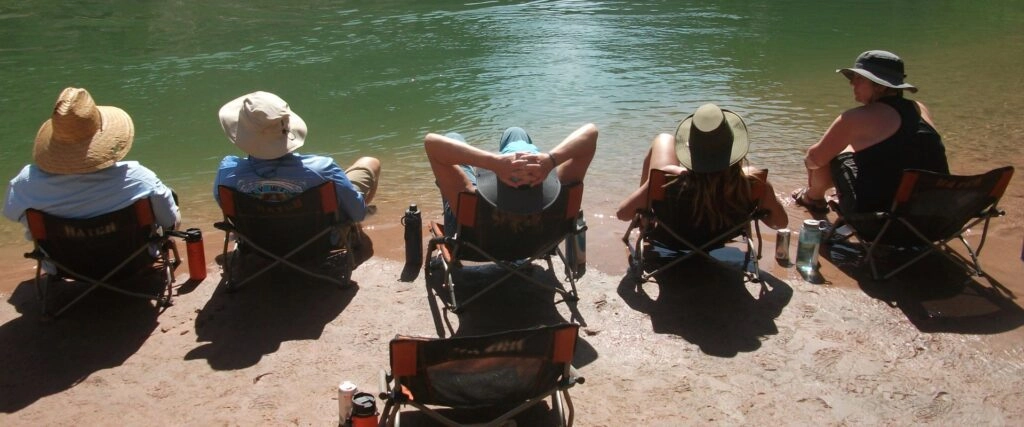 Side Hikes on a Grand Canyon River Trip: What You Need to Know 8 People relaxing at the waters edge in camp chairs by the Colorado River in Grand Canyon