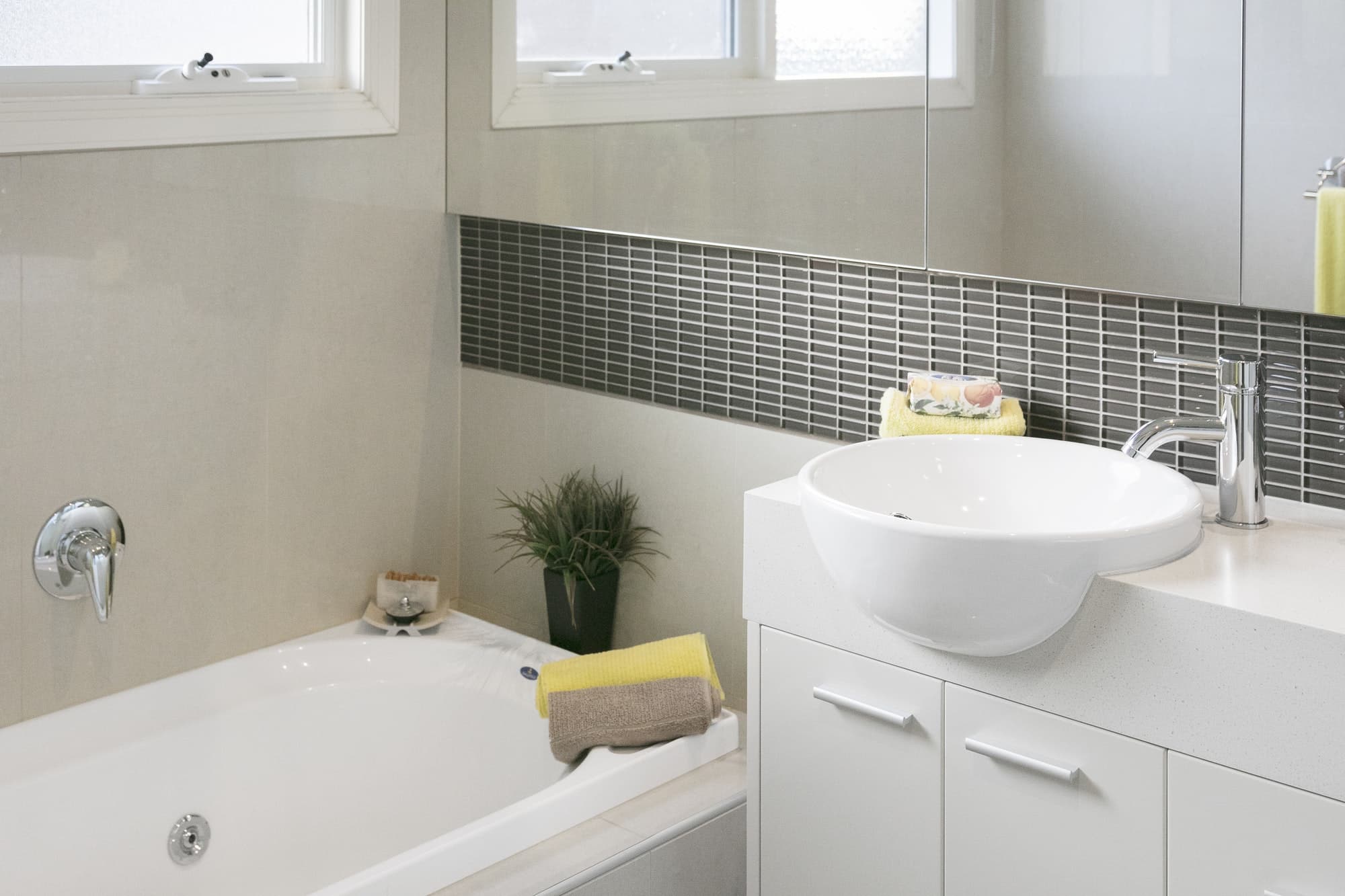 KL Plomberie Services Salle de bain moderne avec baignoire blanche, lavabo vasque et luminaires chromés, accentuée par un dosseret de carrelage décoratif et un décor minimaliste.