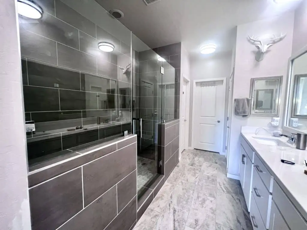 Modern bathroom with gray tile, glass shower, double vanity, and a decorative deer head.