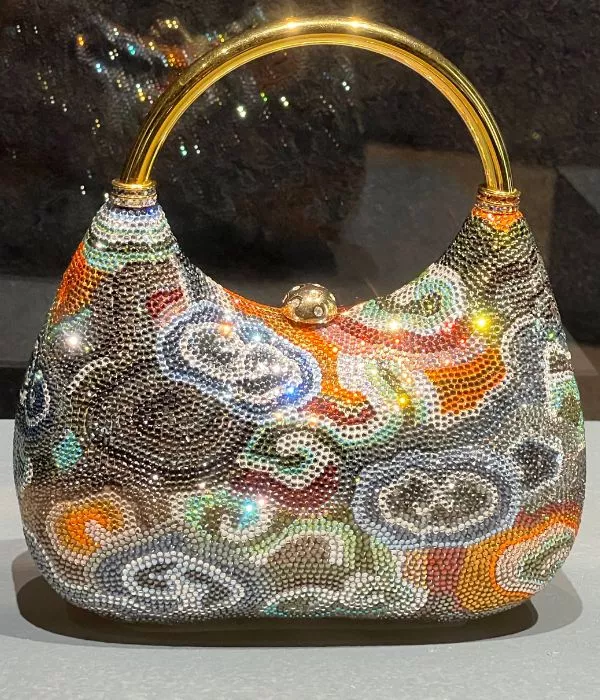 A Multicolored, Intricately Designed Judith Leiber Handbag Adorned With Small, Shimmering Beads And A Gold Handle Is Displayed On A Gray Surface. black prada handbag