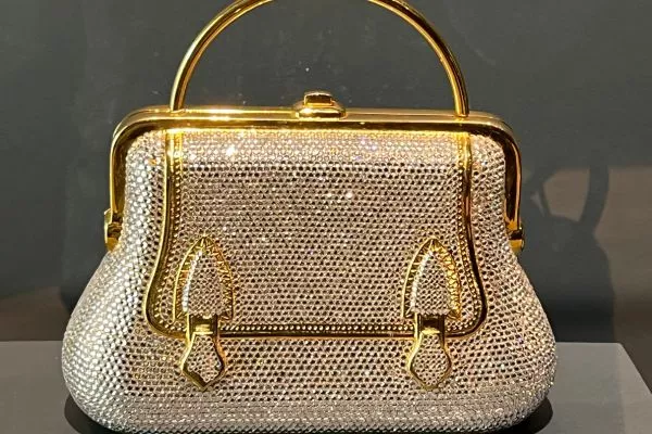 A Judith Leiber Handbag, Adorned With Shimmering Crystals And Gold Accents, Gleams Against A Dark Background. Close Up Of A Prada Handbag On An Acrylic Stand