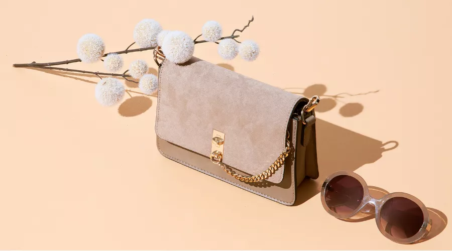 Stylish gray handbag with gold accents and sunglasses, ideal for showcasing seasonal handbag maintenance tips.