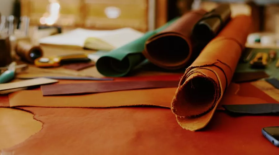 Rolls Of Full Aniline Leather In Various Colors Rest On A Cluttered Workbench, Surrounded By Cutting Tools And Fabric Pieces.