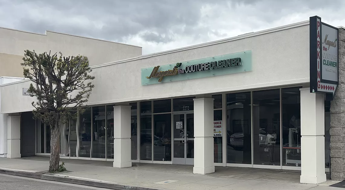 A Storefront With Glass Windows And A Sign Reading “angelus Couture Cleaner” Under A Cloudy Sky; A Parking Sign Is Visible On The Right And A Pruned Tree Stands On The Sidewalk. A Storefront With Glass Windows And A Sign Reading "angelus Couture Cleaner" Under A Cloudy Sky; A Parking Sign Is Visible On The Right And A Pruned Tree Stands On The Sidewalk.