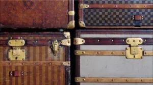 A Close Up View Of Six Vintage Designer Trunks With Brass Hardware, Featuring Various Patterns And Colors, Stacked Tightly Together.