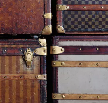 A Close Up View Of Six Vintage Designer Trunks With Brass Hardware, Featuring Various Patterns And Colors, Stacked Tightly Together.