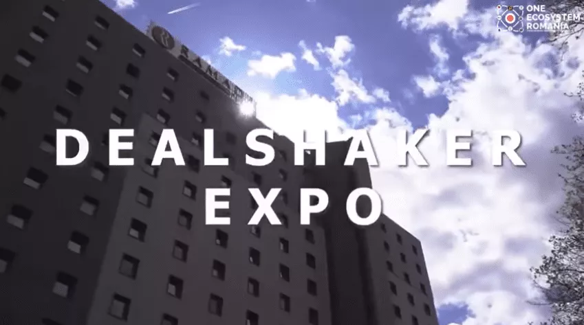 明るい空の下にある建物。大きな白い文字で「DealShaker Expo」と右上隅に「One Ecosystem Romania」のロゴが入っています。このイベントはルーマニアのイベントの真のハイライトです。