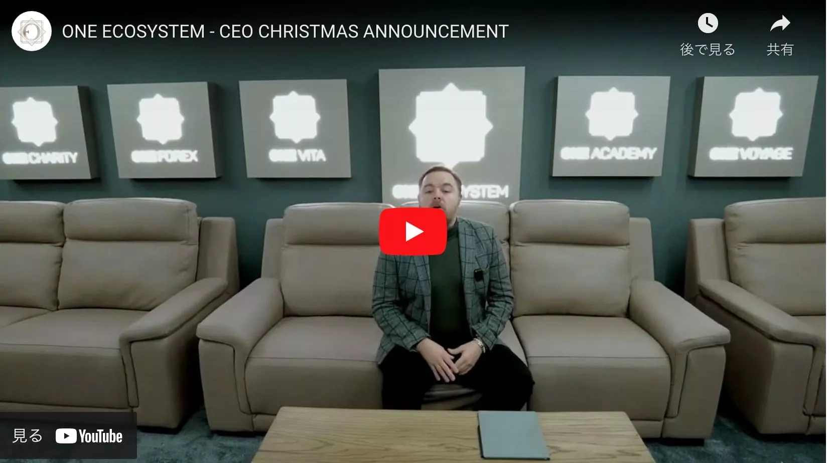 ONE ECOSYSTEM ã®å„部門ã®ãƒã‚´ãŒå…‰ã‚‹å£ã®å‰ã®ã‚½ãƒ•ã‚¡ã«åº§ã‚Šã€CEO ã®å¹´æœ«å¹´å§‹ã®ç™ºè¡¨ã®æº–備をã—ã¦ã„る人物。