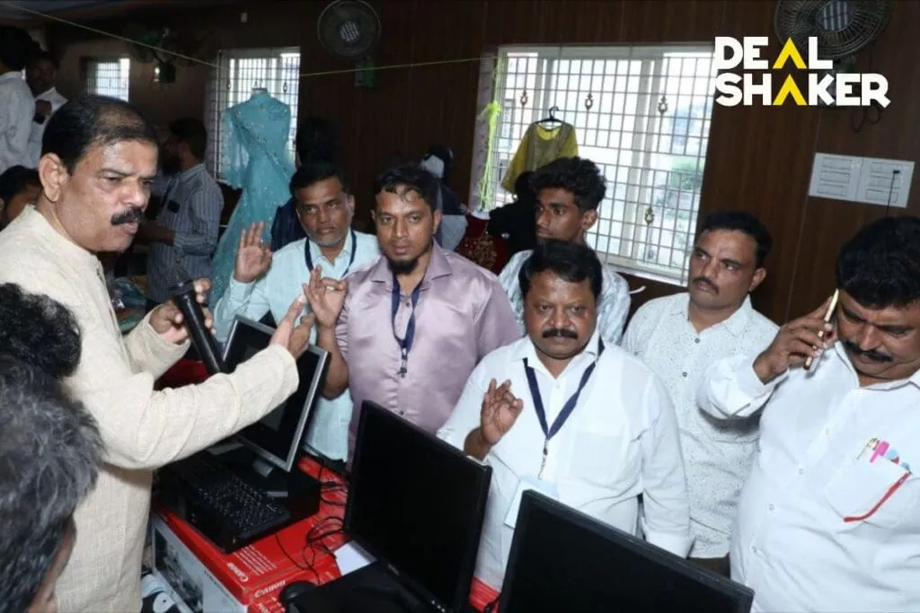 IMAイベント中、ある部屋でコンピューターの周りに立っている男性グループに話しかける男性。何人かの男性が手を挙げて、次に提示される DealShakerエキスポに興味を示しました。