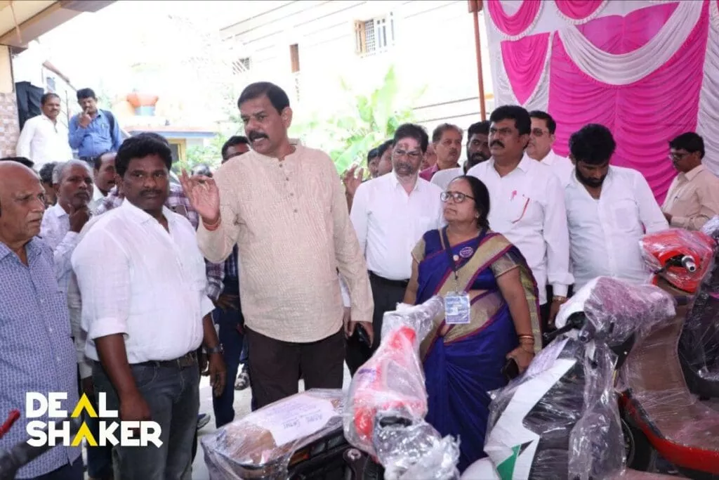 IMAイベントのカラフルなテントの下に集まり、駐車されたバイクに囲まれるグループ。男性が出席者に話しかけ、この注目すべきイベントに組み込まれたエキサイティングな DealShaker エキスポの要素を強調しています。