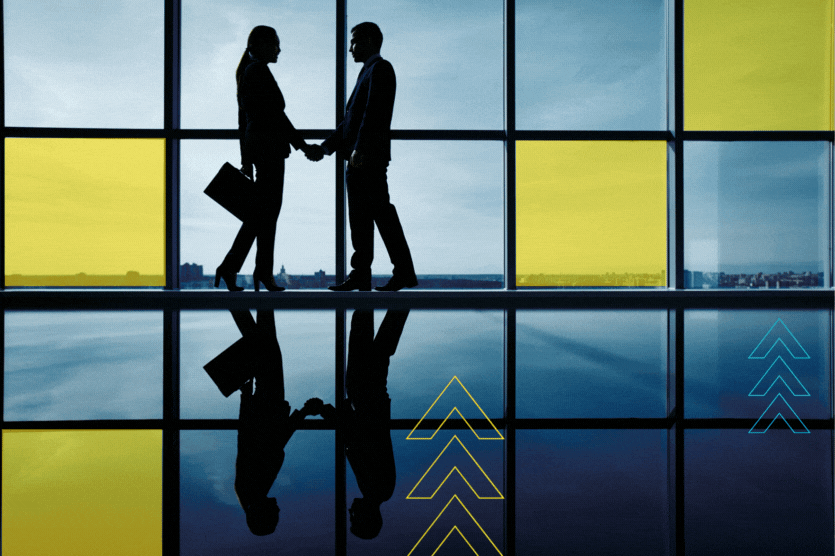 青と黄色のパネルが貼られた大きな窓の前で握手するビジネスウェアの男女のシルエット。右下にはDealShaker加盟店の条件を示す矢印のグラフィック。.