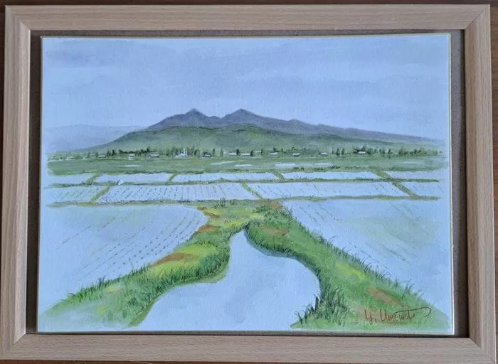 前景に水田、中央に家並み、そして柔らかな青空の下に背景にそびえる山形雫石の緑の山々をフィーチャーした額入り風景水彩画。.