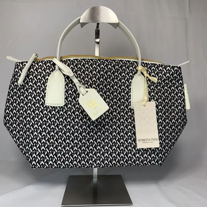 白の持ち手とタグが付いた黒と白の柄のミニダッフルハンドバッグが、無地の明るい背景の金属製ディスプレイスタンドに吊るされている。バッグにはイタリア製であることを示す「ROBERTA PIERI」のラベルが貼られている。.
