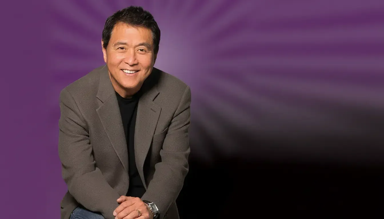 A man with short dark hair, wearing a grey blazer over a black shirt and blue jeans, sits smiling with hands clasped. The purple background features a radial burst pattern, fading to black—perfect for a Rich Dad Poor Dad review or financial education content.