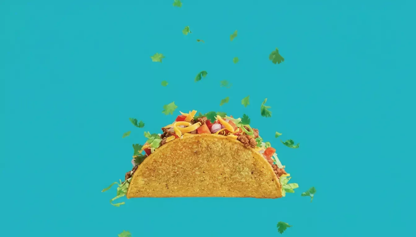 A hard-shell taco filled with seasoned ground beef, shredded lettuce, diced tomatoes, shredded cheese, and chopped onions sits against a bright blue background—a perfect pic for any teen cookbook as pieces of fresh cilantro fall around it.