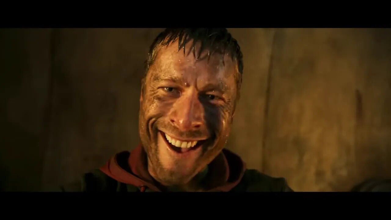 Close-up of a sweat- and dirt-covered man smiling defiantly in dim light