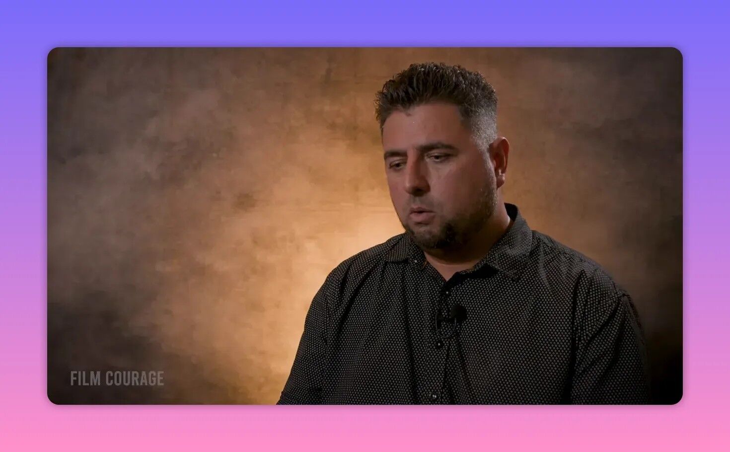 Pensive interview frame of the filmmaker against a warm textured backdrop, looking down and reflective.