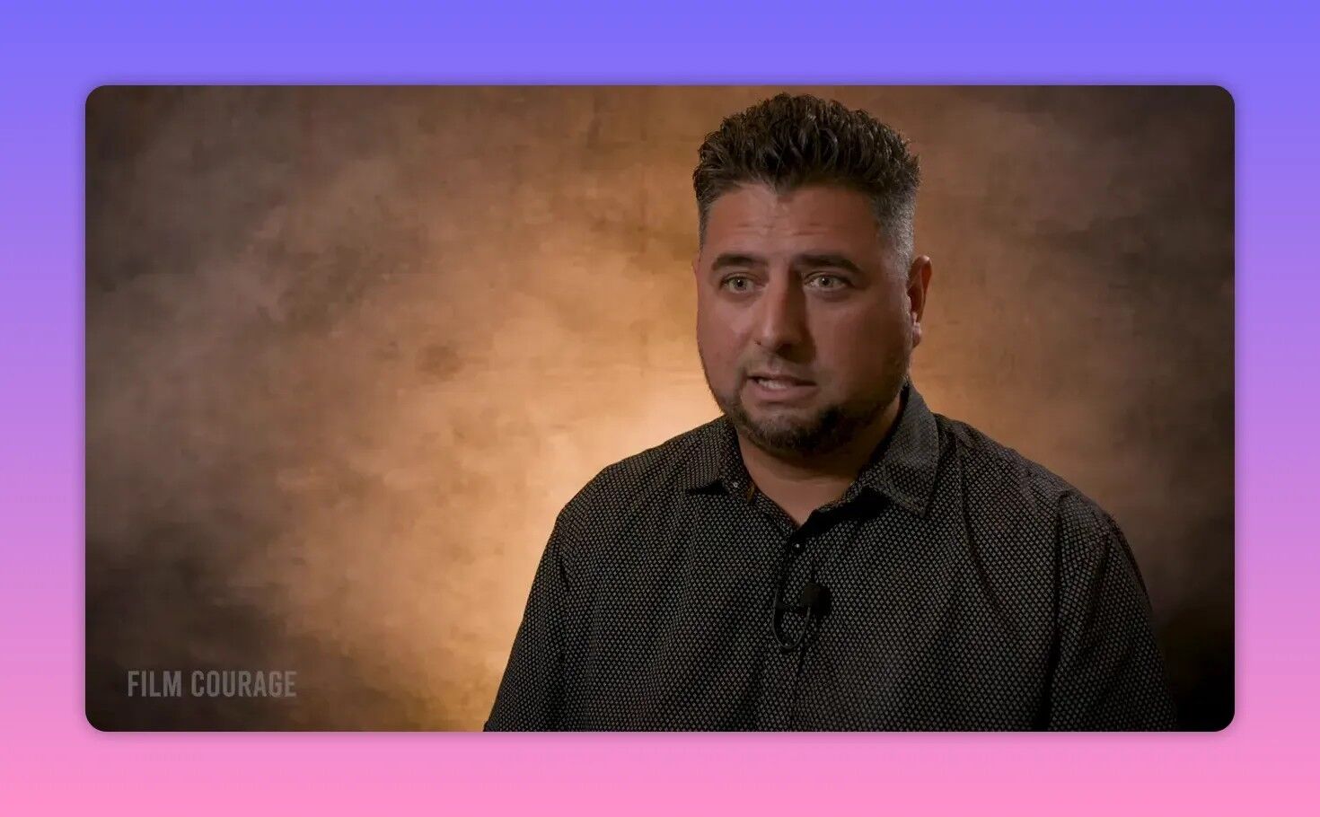 Interview subject in studio against warm textured backdrop, looking forward and mid-sentence with an engaged expression.