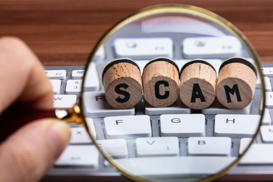 letter tiles spelling out the word scam on a keyboard with a magnifying glass over the letters
